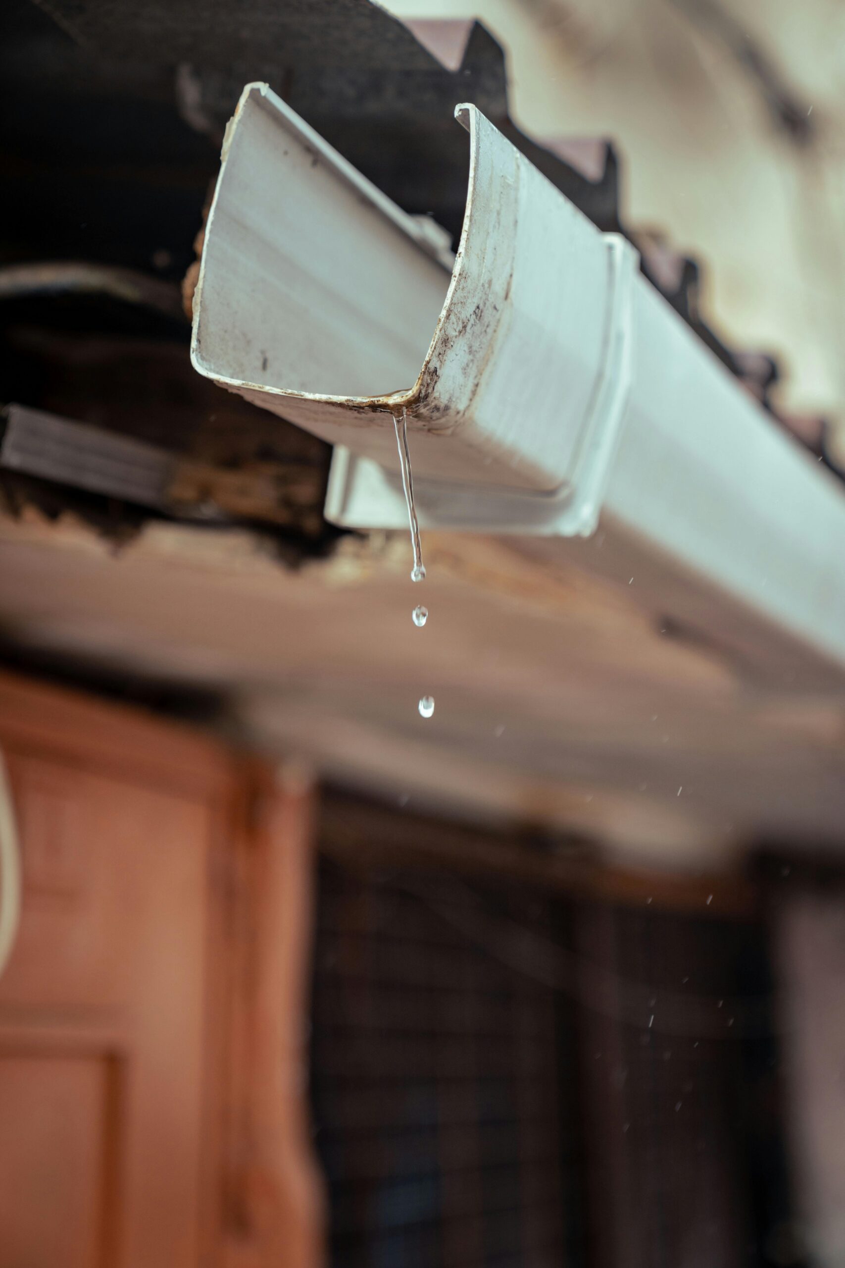 Home Detailed shot of rainwater droplets falling from a house gutter, emphasizing water flow.